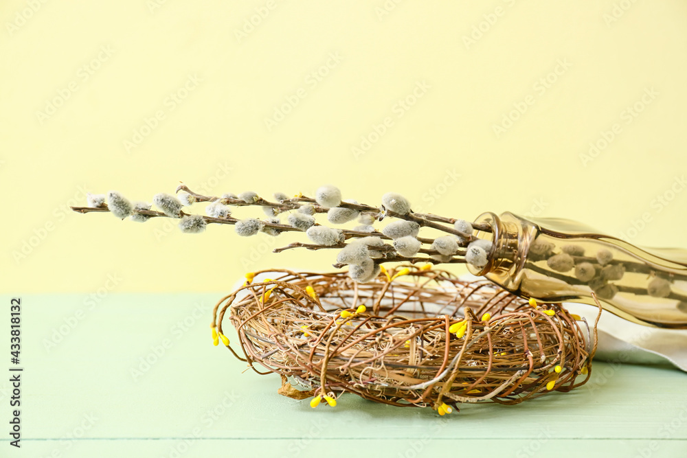 Vase with willow branches and nest with quail eggs on color wooden table