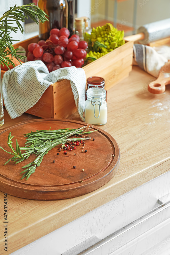 Cutting board with rosemary, peppercorns and different products on kitchen table