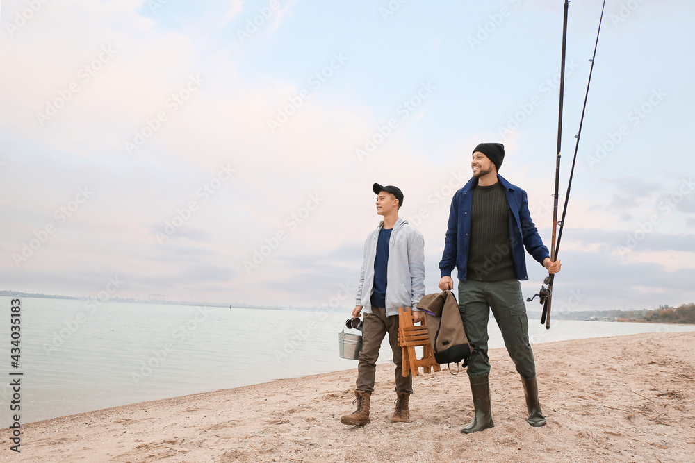 Father and son with fishing equipment walking on riverside