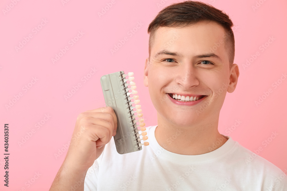 Young man with teeth color chart on pink background