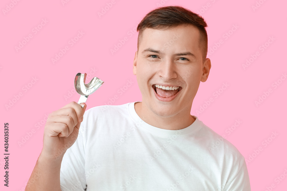 Young man with dental tool for making mold of teeth on color background