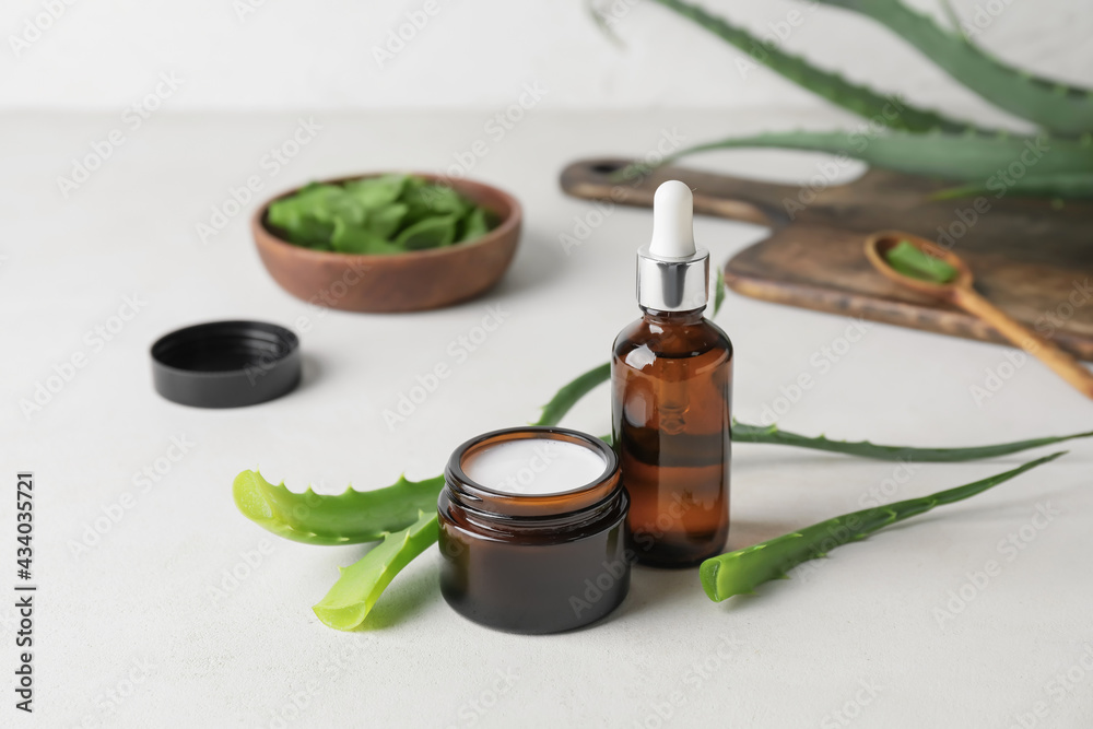 Bottle of essential oil, jar with cream and aloe pieces on light background