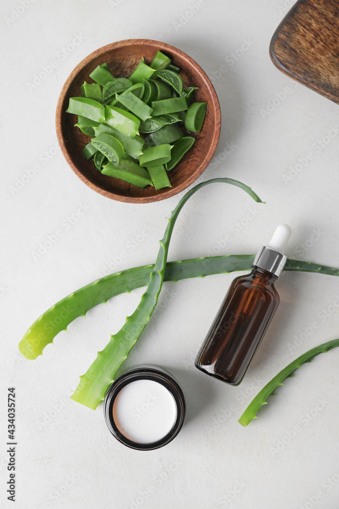 Bottle of essential oil, jar with cream and aloe pieces on light background