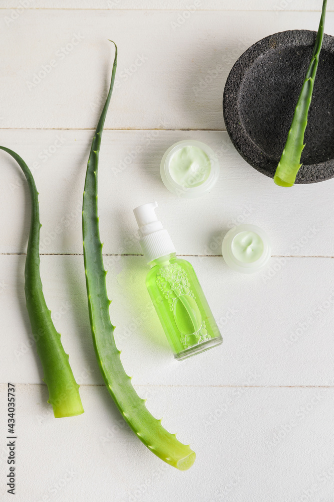 Cosmetic products with aloe leaves on light wooden background