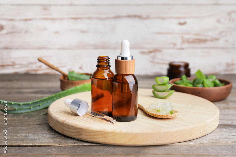 Bottles of essential oil and spoon with aloe on wooden background