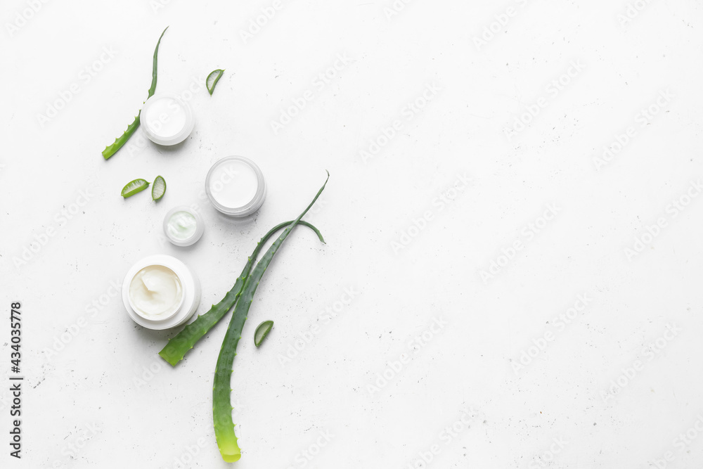 Jars with natural cream and aloe pieces on light background