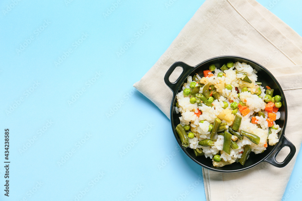 Frying pan with cooked vegetables and rice on color background