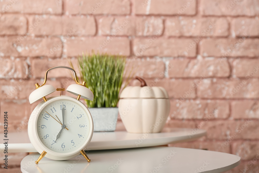 Alarm clock on table near color brick wall