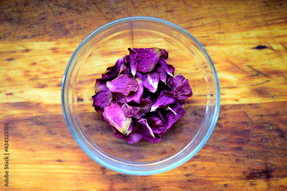 purple rose petals in glass bowl on wooden table - close up