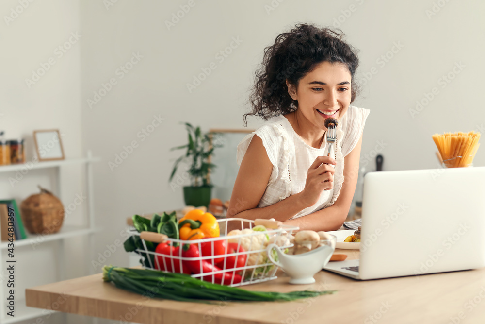 年轻女子在厨房吃饭时使用笔记本电脑