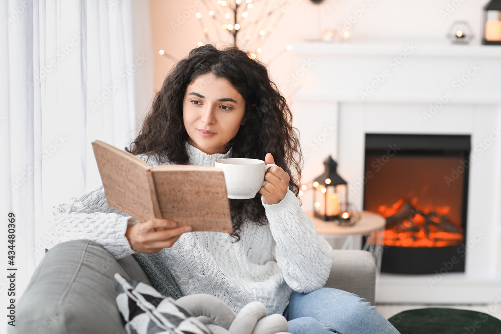 漂亮女人在家里的壁炉旁喝茶看书