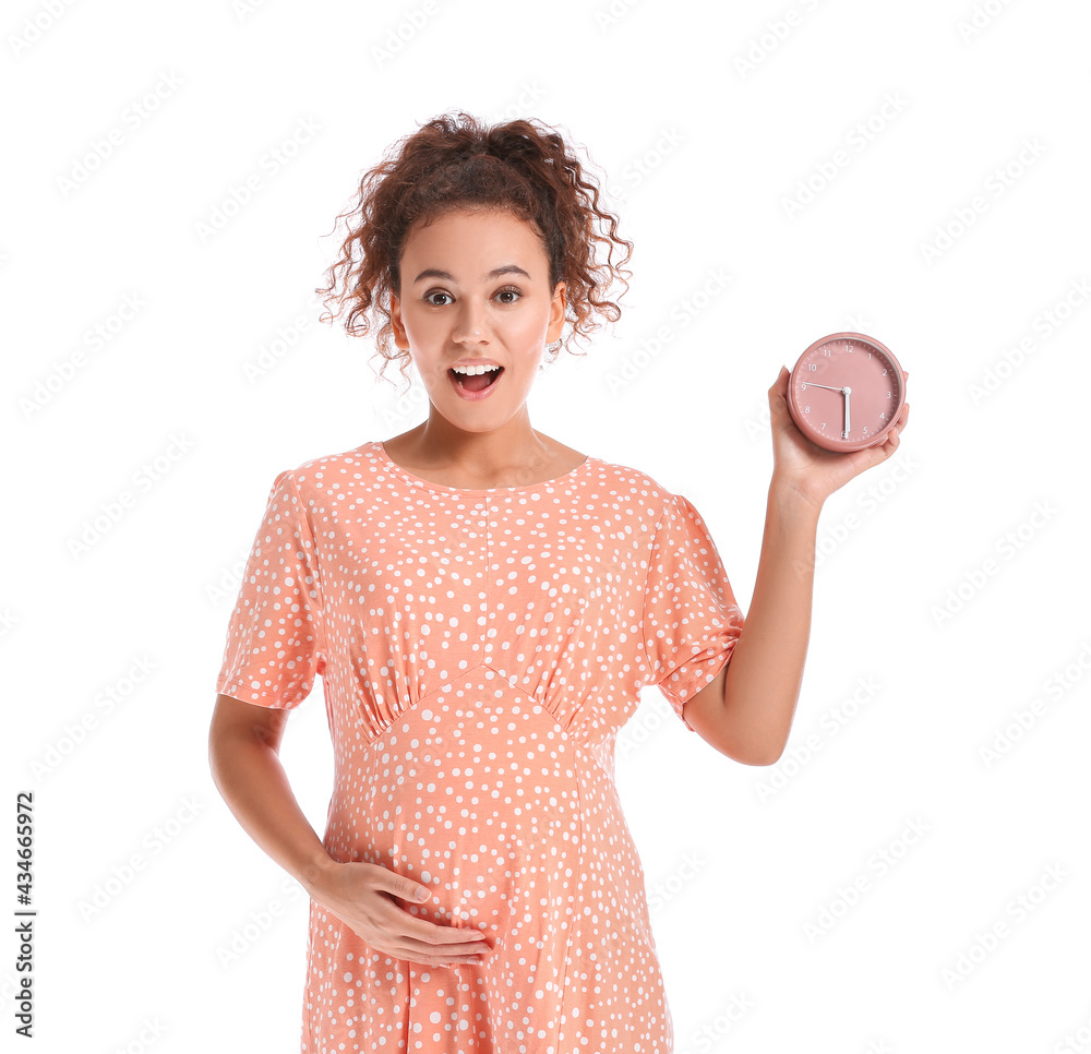 Beautiful pregnant African-American woman with clock on white background