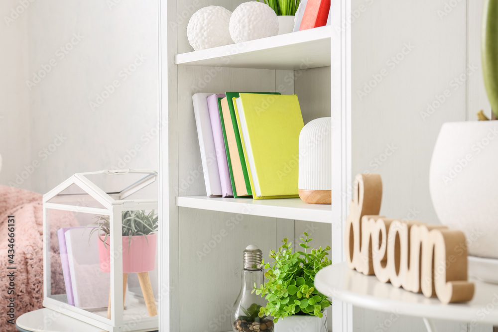 Shelf unit with books and houseplants in interior of light room, closeup