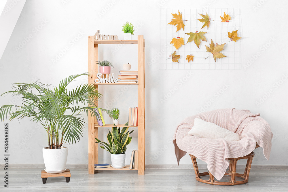 Shelf unit with books, houseplants and armchair near light wall