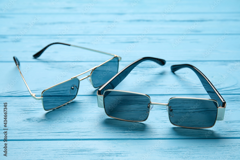 Different modern sunglasses on color wooden background