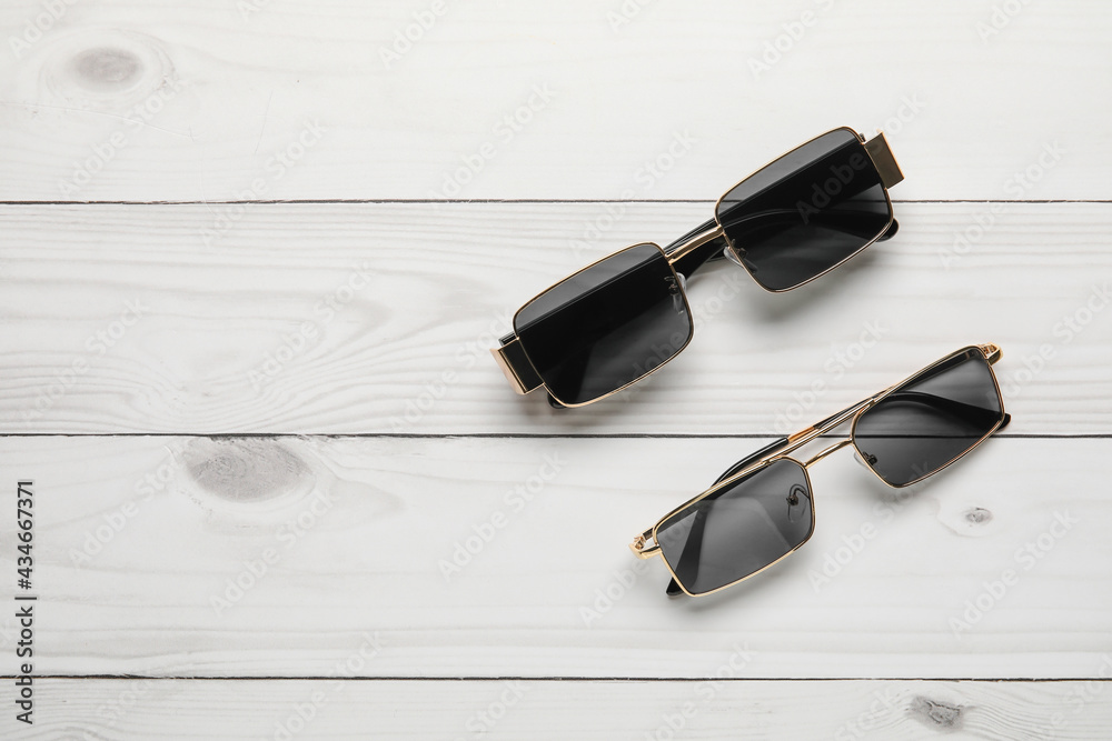 Different modern sunglasses on light wooden background