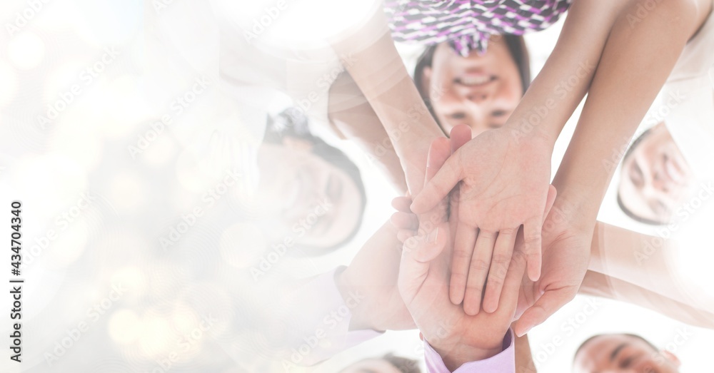 Composition of colleagues smiling and stacking hands with spots of light