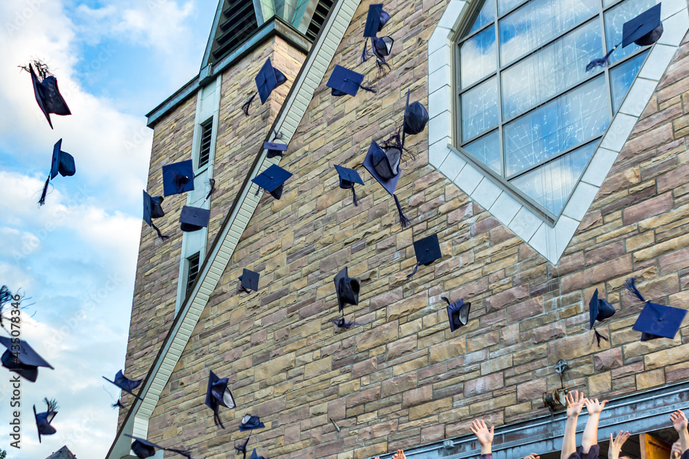 Group of graduating students celebrating their graduation day outdoors while throwing their hats (mo