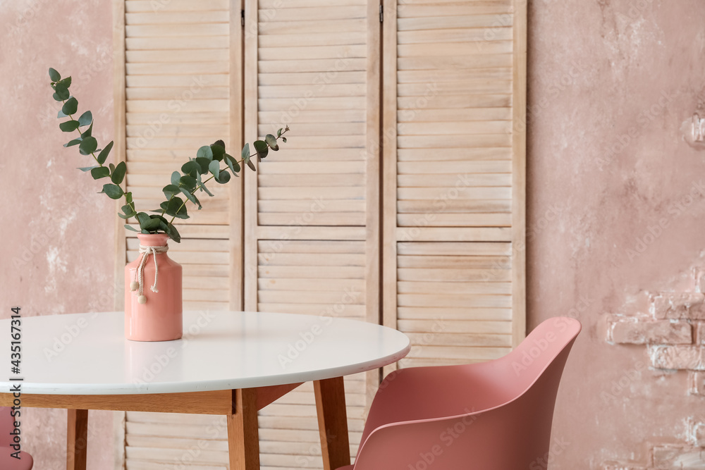 Vase with eucalyptus branches on table and folding screen near color wall