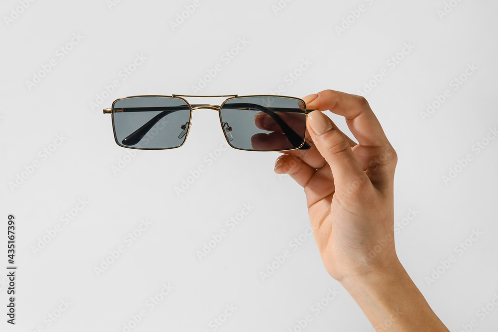 Female hand with stylish sunglasses on light background