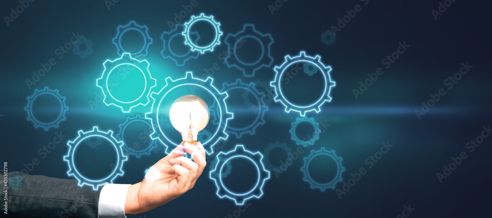 Start up and idea concept with digital gears and glowing light bulb in man hand on abstract dark bac