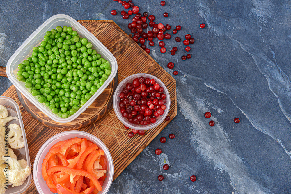 Plastic containers with vegetables and cranberry on color background