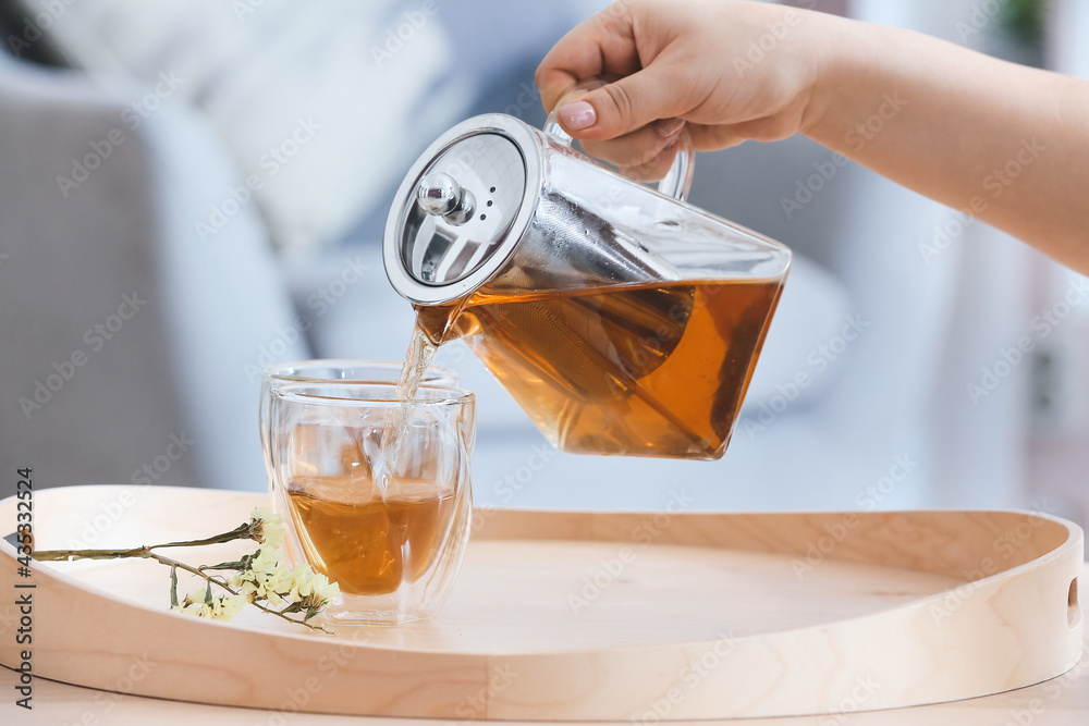 Woman pouring hot tea from teapot into glass in room