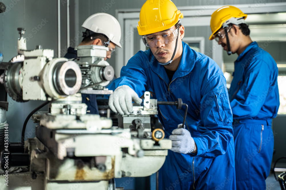 Asian male mechanical worker working on milling machine in workshop.