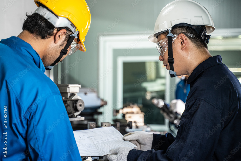 Asian male engineer explaining job to mechanical worker in workshop.