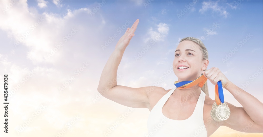 Composition of athletic female medalist raising hand over blue sky and clouds