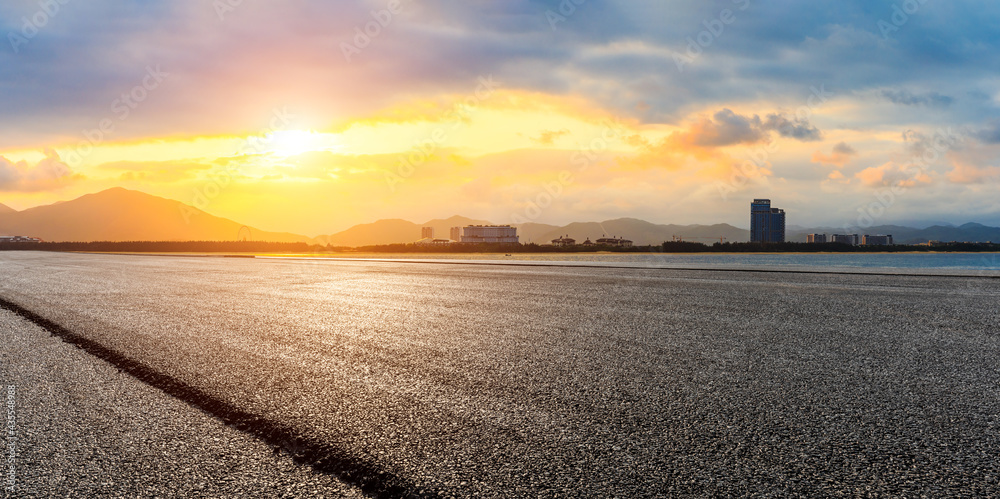 Empty asphalt road and city skyline with mountain at sunset.