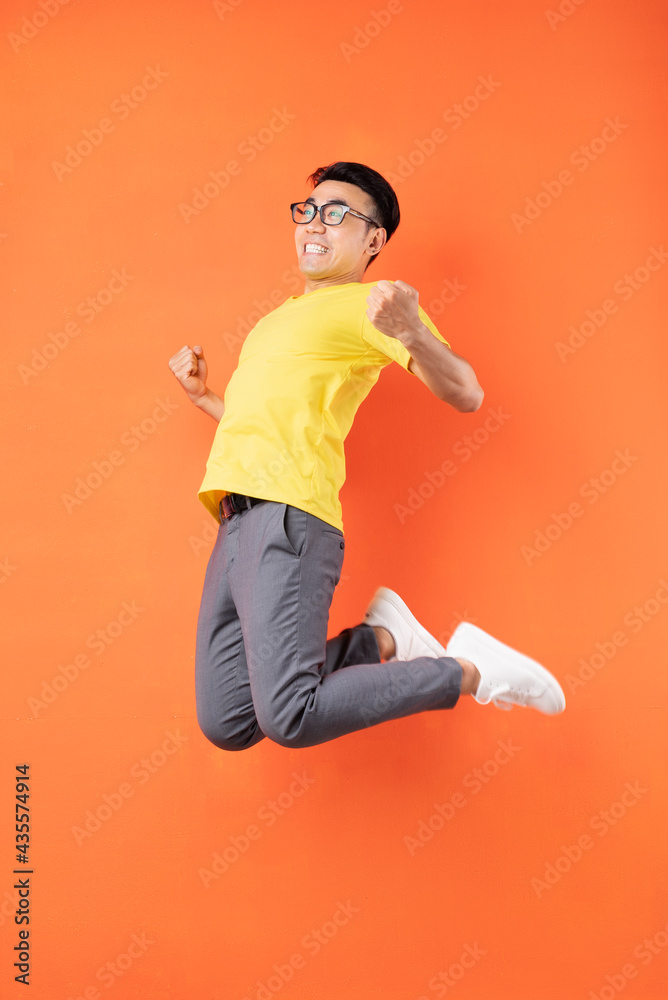 Asian man in yellow t-shirt jumping on orange background