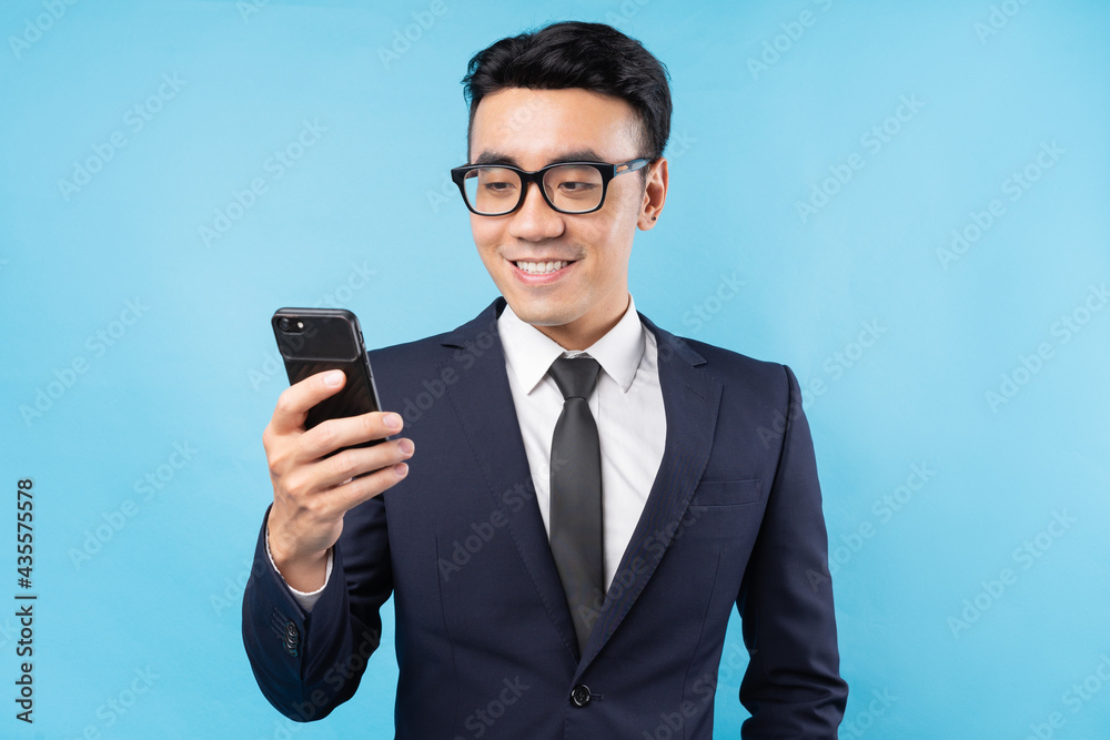 Asian buisnessman wearing suit holding smartphone on blue background