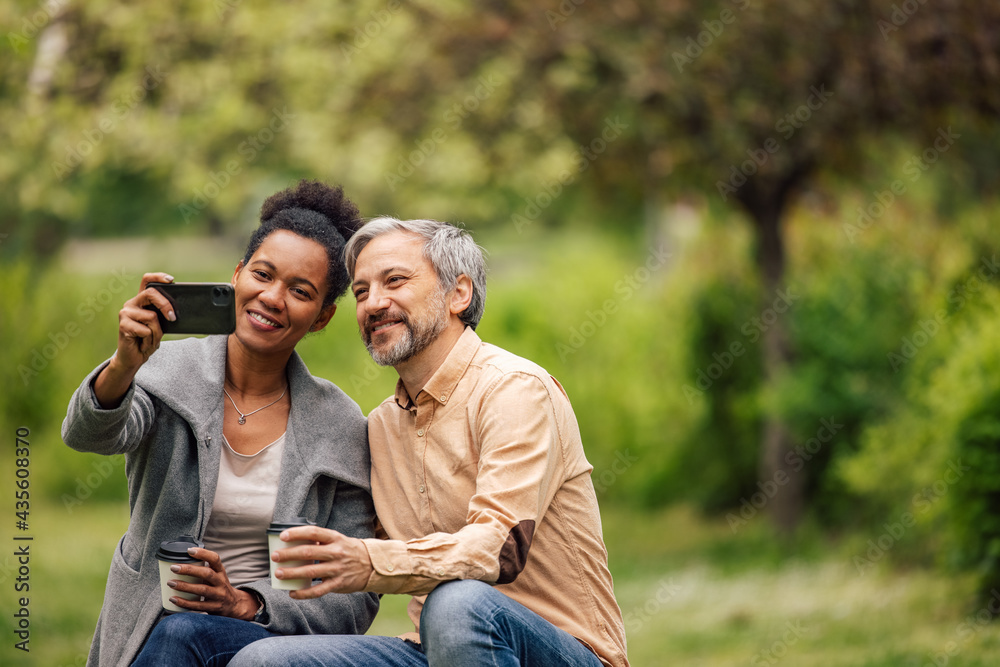 Adult couple making photos in the park, while drinking coffee.