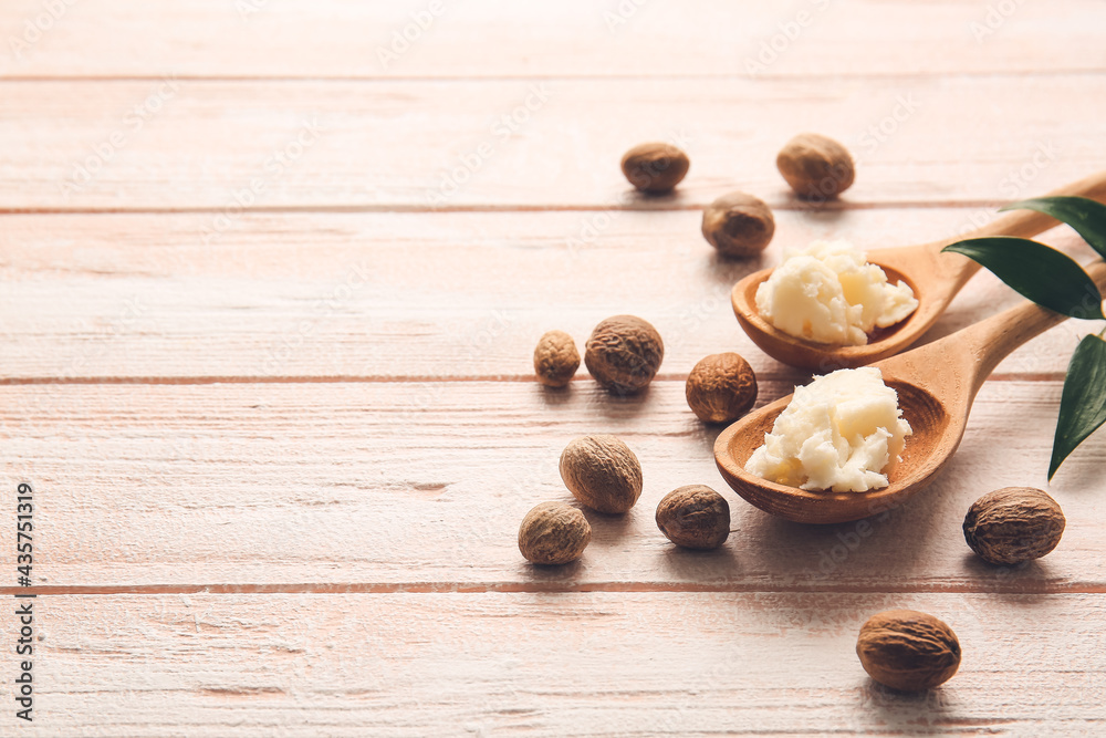 Spoons with shea butter and nuts on light wooden background