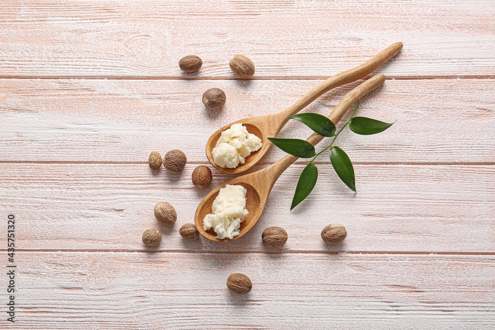 Spoons with shea butter and nuts on light wooden background