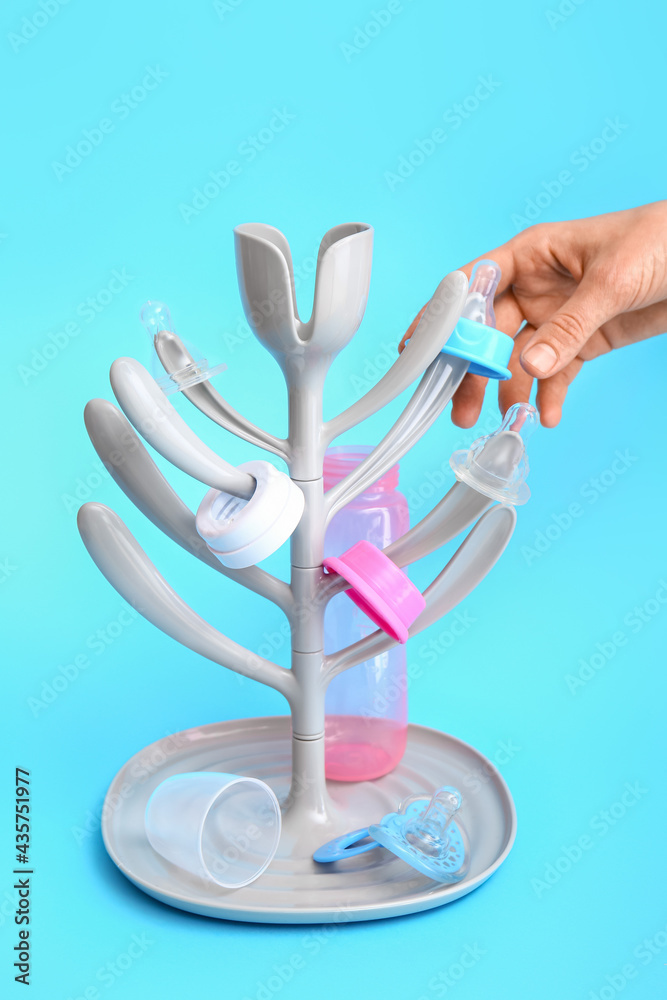 Female hand and drying rack for baby bottles on color background