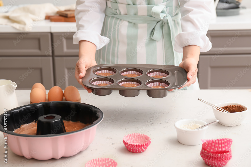 Woman with uncooked cupcakes in kitchen