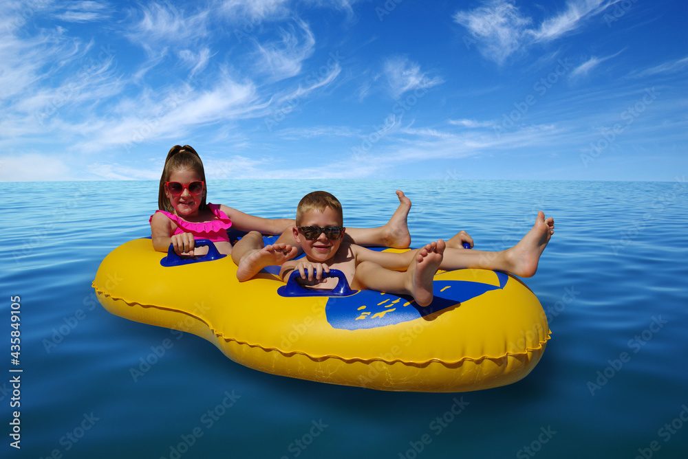 Boy and girl on inflatable float in blue sea water.