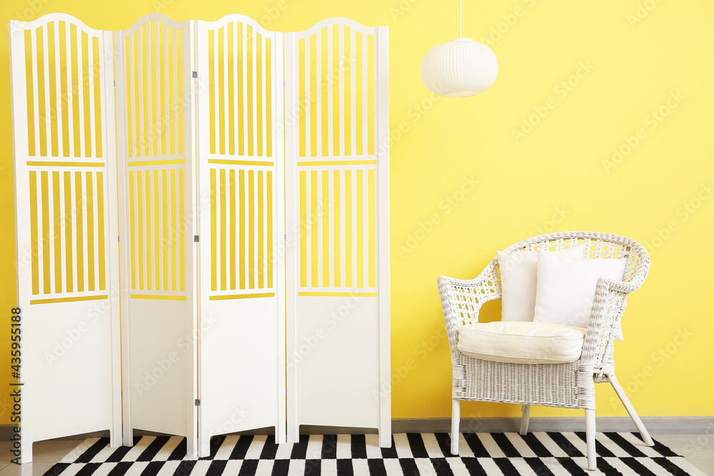 Stylish folding screen and armchair near color wall