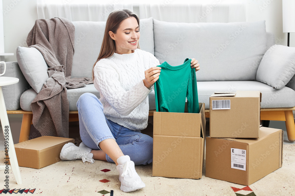 Young woman opening parcel with new clothes at home