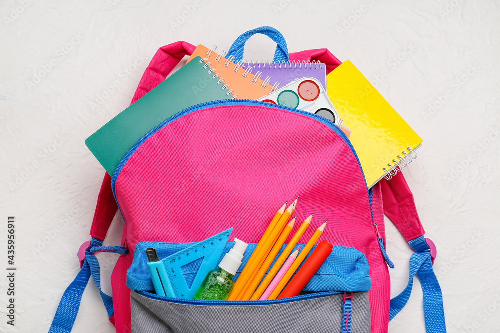 School backpack and stationery on light background