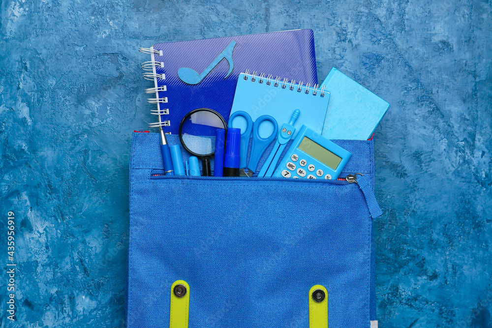 School backpack and stationery on color background