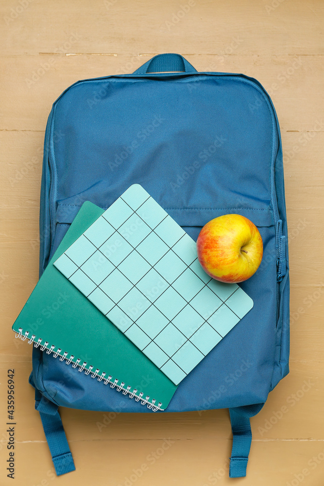 School backpack, apple and notebooks on color wooden background