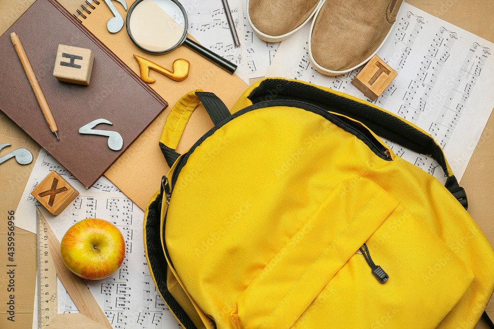 School backpack, stationery and music sheets on color background