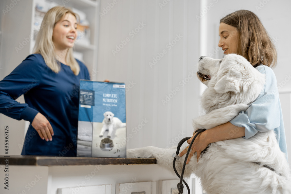 Female owner with big white dog on reception in veterinary clinic choosing dry food for the pet. Dog