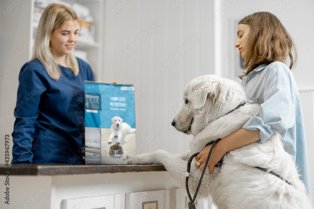 Female owner with big white dog on reception in veterinary clinic choosing dry food for the pet. Dog