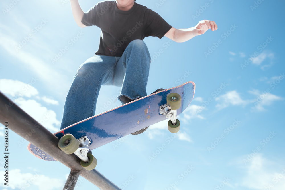 Teenager skateboarder does an ollie trick on background of blue sky gradient