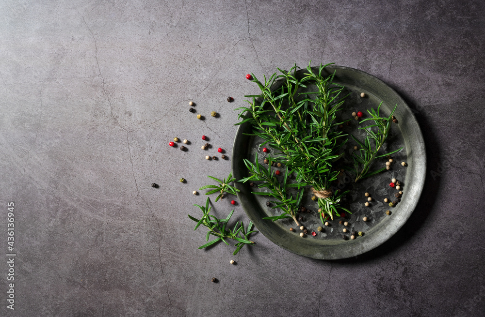 A bunch of fresh rosemary and pepper mix on an iron plate set against a dark background