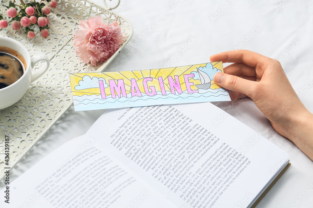 Woman with cute bookmark and book on bed